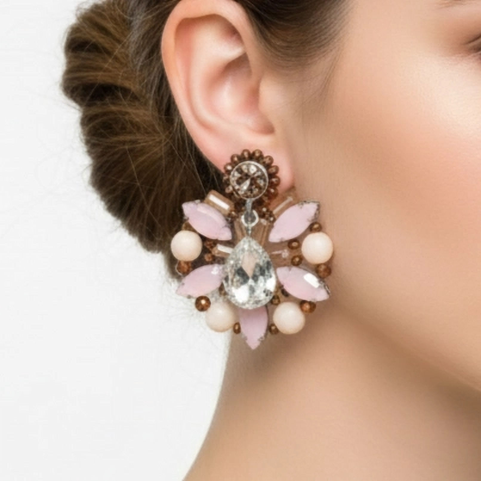 Large stud earrings with a central teardrop crystal and crystals in various shades of brown and pink, on a model's earlobe.