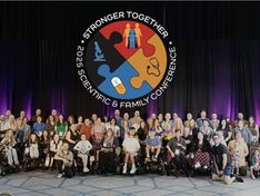 A large group of families, scientists, and advocates pose together in front of a stage with purple lighting. A big circular conference logo with puzzle pieces, medical icons, and the words “Stronger Together – 2025 Scientific & Family Conference” is displayed above them.