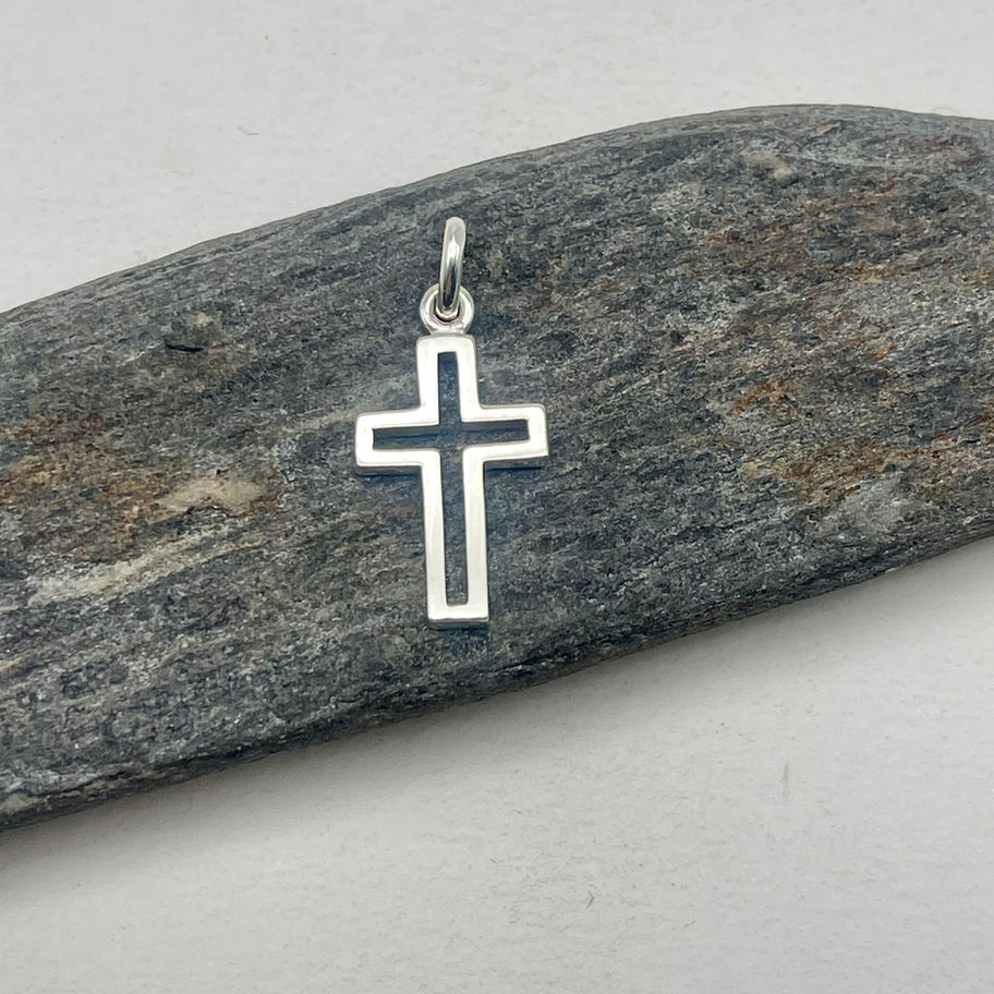 Handmade silver open cross pendant displayed on a rustic wooden surface, showing the clean minimalist cross outline.