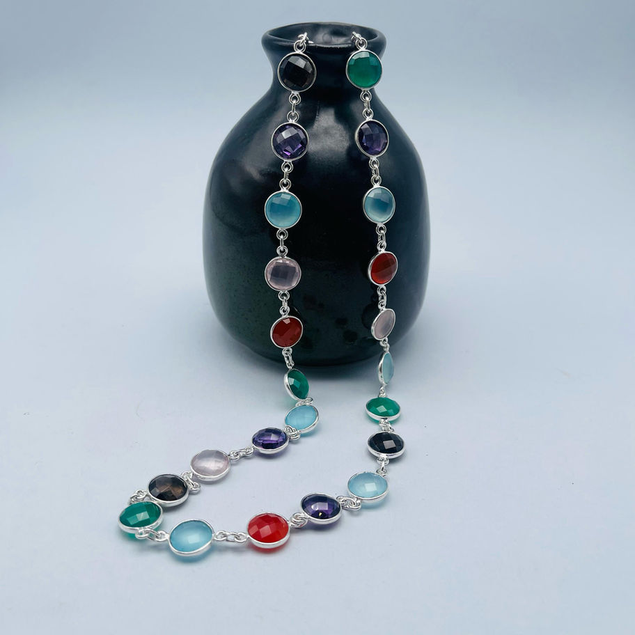 Multi gem long necklace with colourful gemstones displayed against a dark ceramic vase.