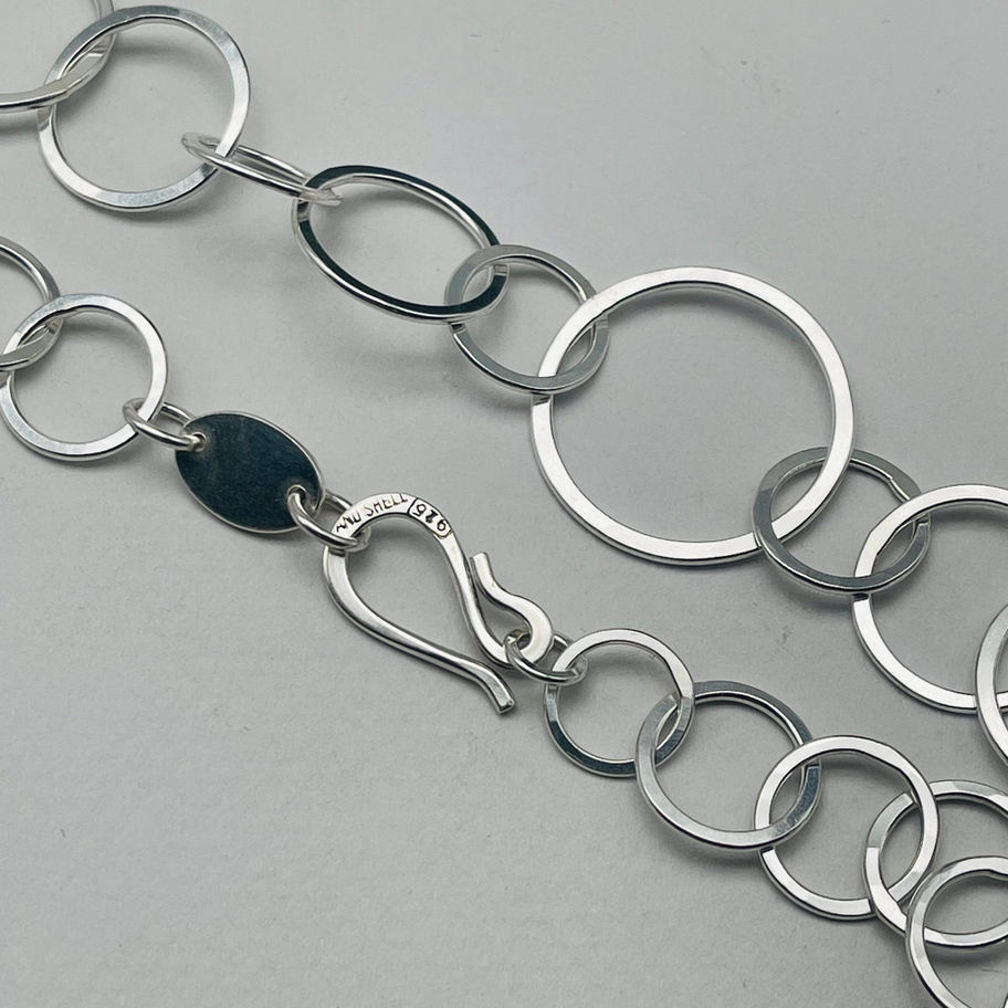 Close-up of the round link necklace, showing mixed-size silver links and the clasp detail.