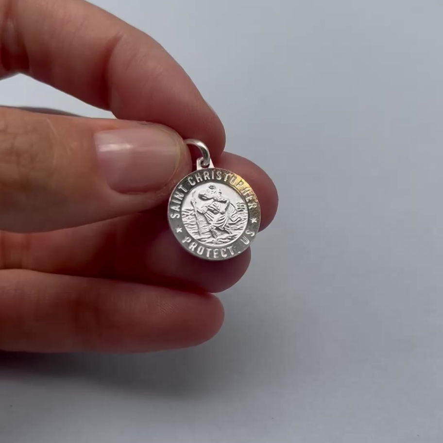 Saint Christopher Protect Us pendant held between fingers, showing the small round silver charm.