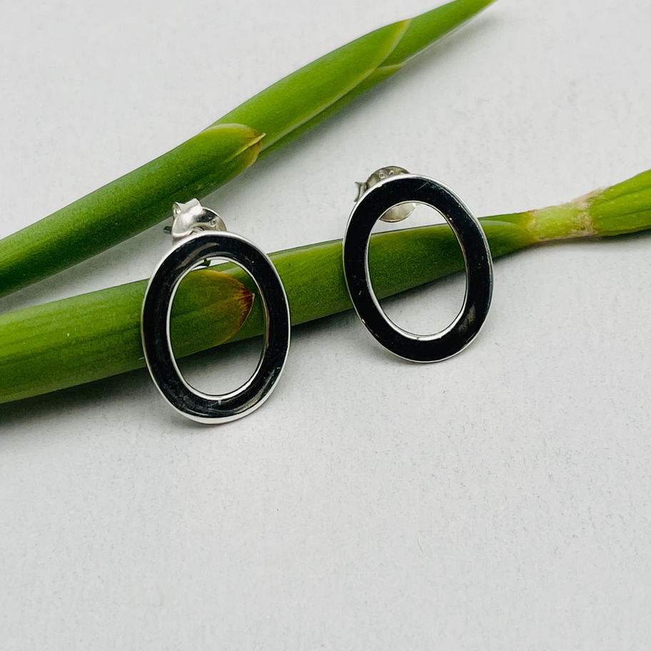 Handmade silver open oval stud earrings displayed with green stems, showing the polished oval shape.