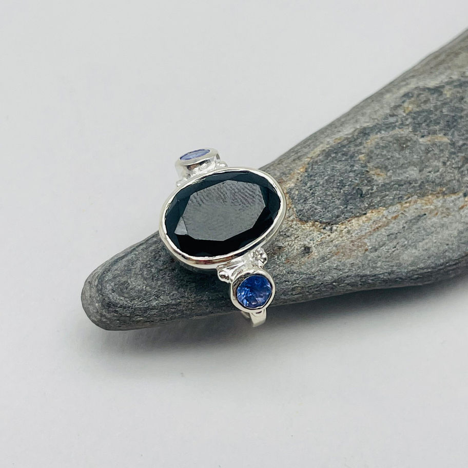 Handmade silver faceted onyx ring displayed on a grey stone surface.