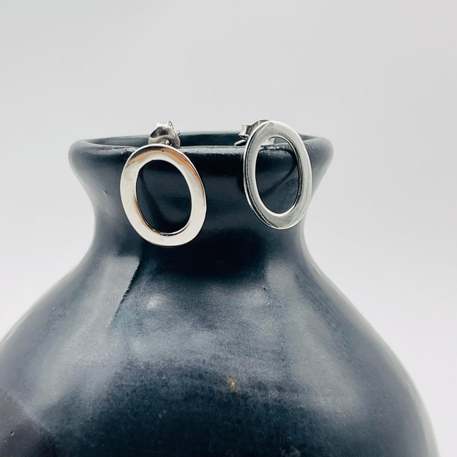 Open oval silver stud earrings displayed on a dark ceramic vase, highlighting the minimalist design.
