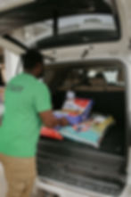 A Manning’s Feed and Seed staff member wearing a green "STAFF" shirt loads large bags of poultry feed, including Kalmbach Henhouse Reserve, into the back of a white SUV for a customer.