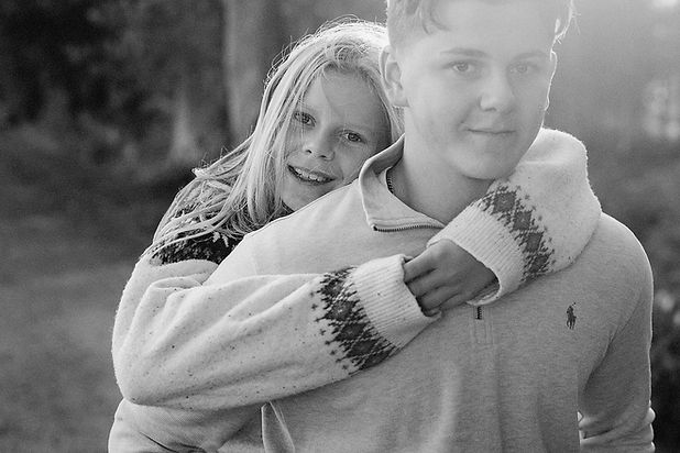 lilla syster kramar sin stora tonårsbror bakifrån medan de båda tittar i kameran