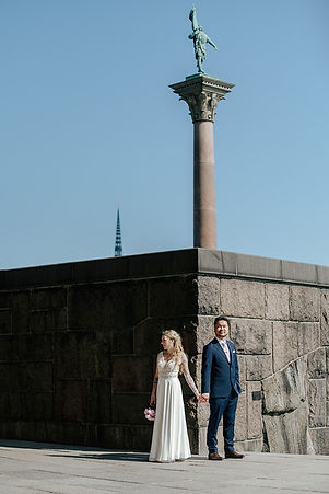 en kontrastrik bild på ett bröllopspar vid Stockholms rådhus, tjejen i vit klänning är mot en nästan svart bakgrund, medans brudgummen i mörkkostym står mot en solbelyst vägg