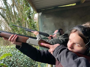 Woman and man aim shotguns at an outdoor shooting range under a shelter, focused and concentrated on target practice.
