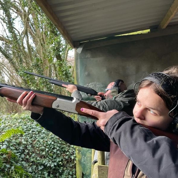 Woman and man aim shotguns at an outdoor shooting range under a shelter, focused and concentrated on target practice.