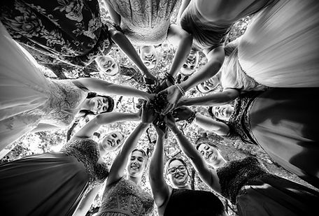 Schwarz weiss Foto: Brautjungfern stehen bei einer Hochzeit im Kreis, strecken die Hände zusammen und lachen, Blick von unten.