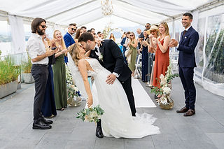 Das Brautpaar küsst sich beim Dip im Mittelgang, umgeben von jubelnden Gästen unter einem 