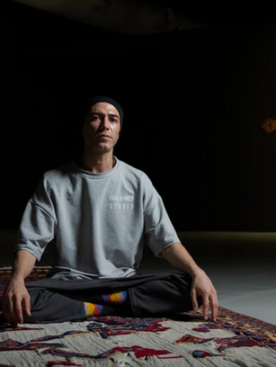 Faig Ahmed, Azerbaijani contemporary artist, standing next to a melting and glitch-inspired traditional Azerbaijani carpet that blends heritage patterns with modern digital distortions.