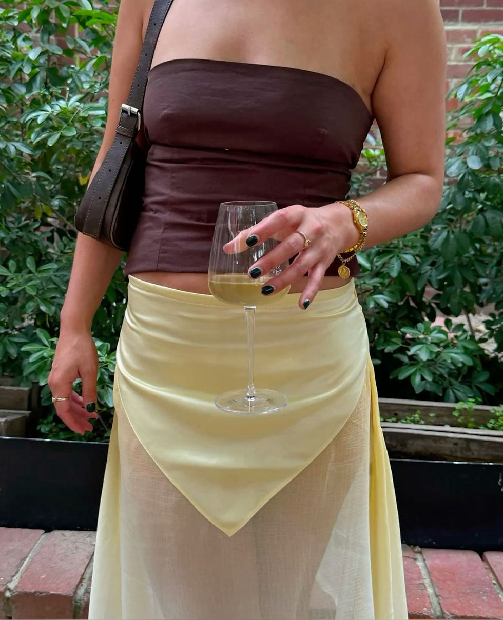 new york fashion girl wearing tube top and yellow stylish skirt holding wine and jewellery