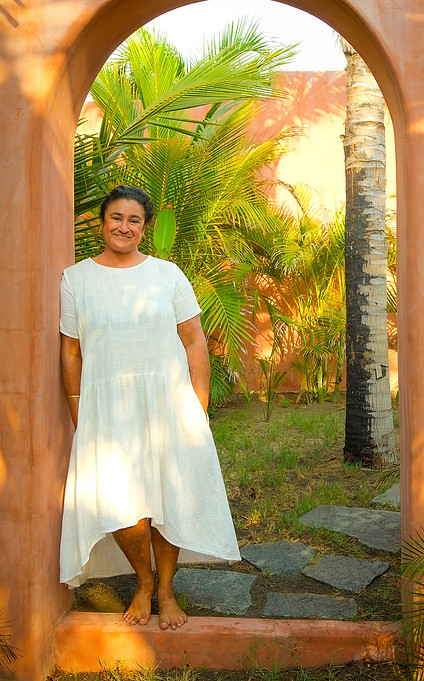 Sonal in a white dress leaning against an arch in a garden
