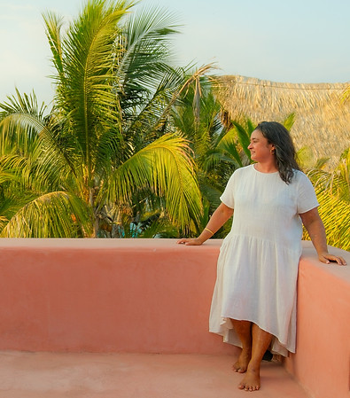 Sonal looking pensive into the distance wearing a white dress perched on a balcony