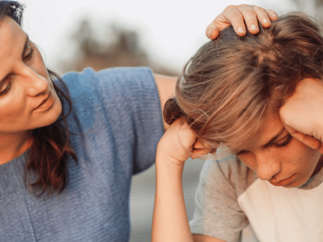 Woman checks a worried child’s head, both leaning close indoors, with a calm but concerned mood.