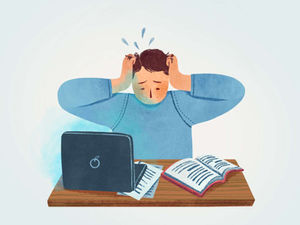 Stressed student clutching head at a desk with a laptop and open book, papers scattered, looking overwhelmed and anxious.