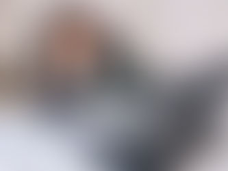 Woman in a checkered jacket sits at a desk looking stressed at a laptop. Charts and papers are scattered around in a bright office.