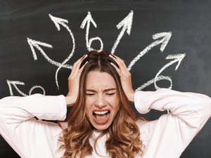 Frustrated woman in a white sweater screams and holds her head before a chalkboard with arrows pointing in many directions