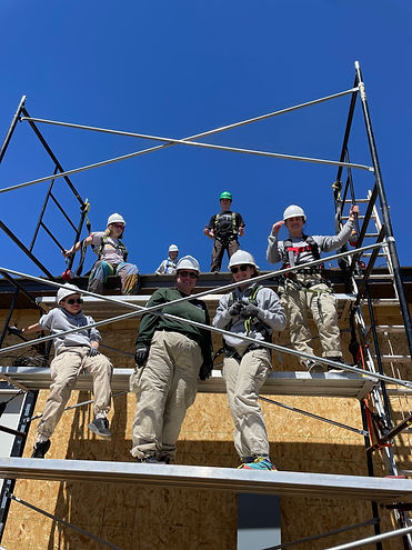 A group of Americorps volunteers standing on several levels of scaffolding, smiling.
