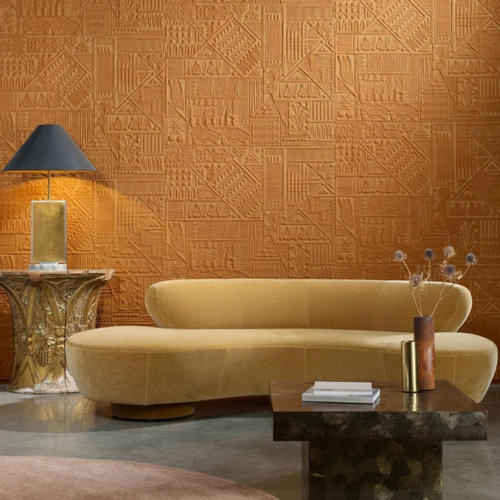 Papier peint Arte relief gravure ethnique ton terracotta ocre, mis en scène dans un salon avec canapé arrondi velours jaune – Atelier Marceau Nice