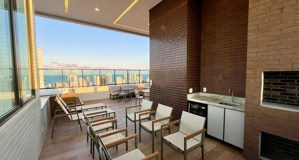 Área Sunset Grill no terraço da cobertura com bancada gourmet e mesas para recepções.