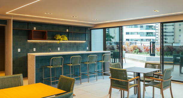 Área interna do espaço gourmet com grande balcão em mármore, banquetas altas, marcenaria de alto padrão e eletrodomésticos embutidos de última geração.