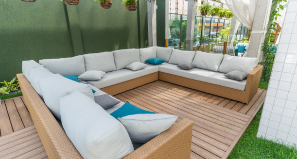 Espaço lounge externo e coberto com sofás confortáveis, almofadas decorativas e mesas de centro, ideal para descanso e conversas.