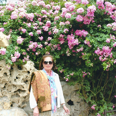 Cristina Piñeiro parada adelante de una gran planta de rosas rosadas