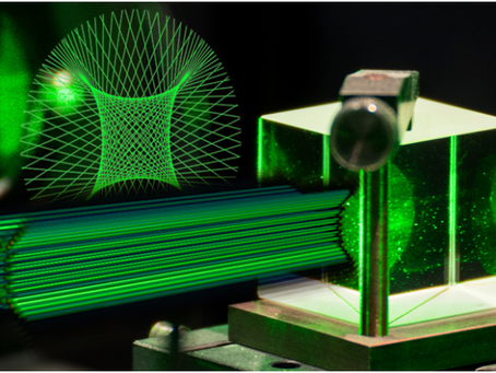 Green laser beams intersect a glass cube on a metal stand, creating geometric patterns. The background is dark, amplifying the vivid glow.