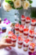 Little layers of red and white in small glasses on a stepped display. A hand is picking one of them up.