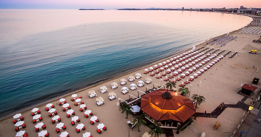 Stunning panoramic view of the Black Sea coastline with a wide sandy beach, elegant sun loungers, calm water, and a beautiful sunset atmosphere, showcasing Varna as an ideal destination for a relaxing seaside escape.