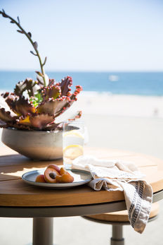 Wood dining table with succulent arrangement, fresh fruit, and linens overlooking the beach and Pacific Ocean.