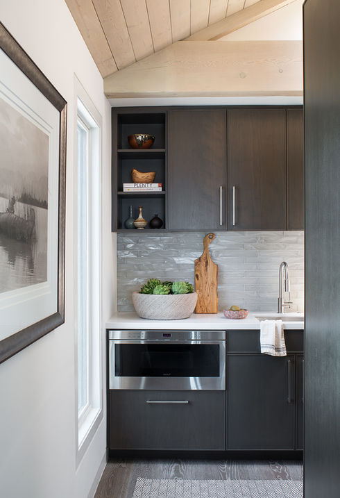 Modern butler's pantry in a coastal home in Playa del Rey, Los Angeles, featuring sleek dark cabinetry, marble backsplash, and wooden ceiling accents.