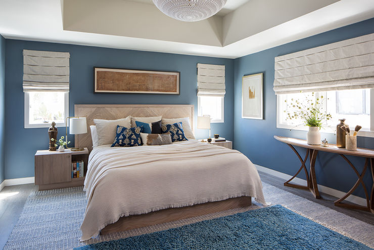 Inviting guest bedroom in a coastal Playa del Rey home, styled with deep blue walls, complementing blue area rug, wooden furniture, and accents of beige and patterned blue pillows, under a decorative ceiling fixture.

