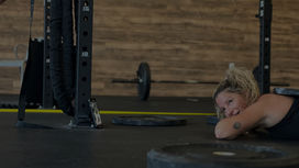 Client at Vital Fitness Lakeland lying on gym floor after a strength and cardio workout. Smiling, with workout equipment around feeling motivated.