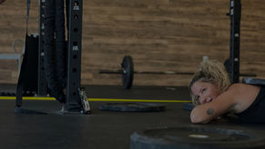 Client at Vital Fitness Lakeland lying on gym floor after a strength and cardio workout. Smiling, with workout equipment around feeling motivated.