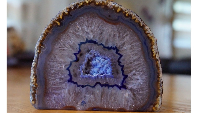 Purple geode slice with concentric bands and crystal center on a wooden surface. Background is soft-focused indoors with diffused light.