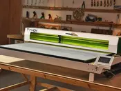 Tyvok K1 on Kickstarter, a white and green 100W CO2 laser engraver, on a wooden workbench in a home workshop.