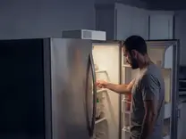Man opening fridge at night during power outage with Sierro home backup unit mounted on top keeping it running