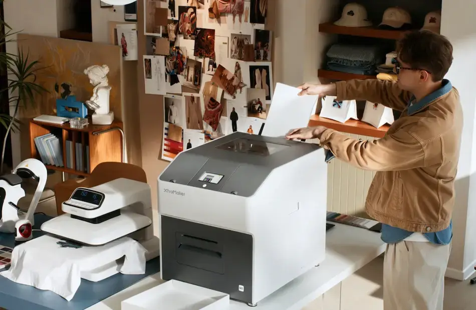 Person operating the XtraMaker M1 DTF printer beside a heat press in a small creative workspace