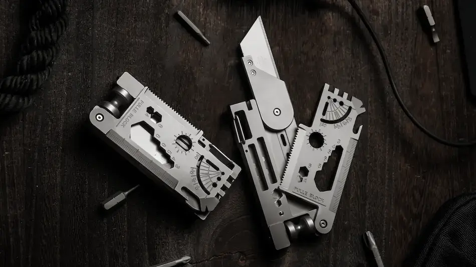 SpinDeck rotating titanium multitool card laid flat showing the deployed utility blade, serrated edge, magnetic driver ports, and engraved ruler