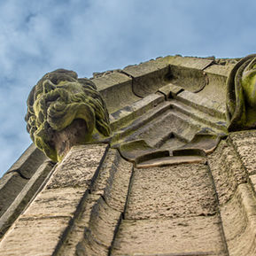 Weathered stone gargoyles on a building, viewed from below