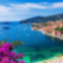 Nice - França: Vista da costa de Nice, França, mostrando o mar azul repleto de barcos, emoldurado por flores vermelhas e roxas em primeiro plano.