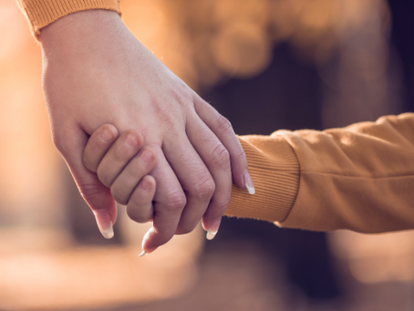 A close-up view of a mother and child holding hands against a natural backdrop of parkland and trees