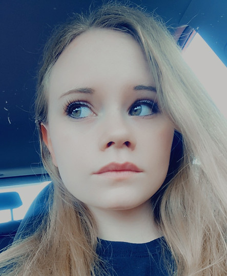 Starrr Reid, a member of Fallen7, looking off to the side with a thoughtful expression. She has long blonde hair.