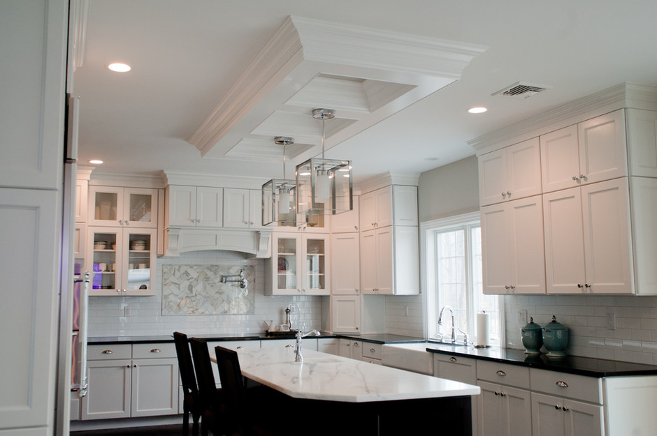 This kitchen design and remodel included installing white cabinetry with a matching white subway tile backsplash. Black countertops surround a white, farmhouse-style kitchen sink, while the kitchen island features espresso cabinetry and a white countertop. The island features an additional sink.