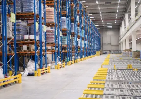 Interior gudang dengan rak selective racking tinggi berisi pallet barang dan jalur conveyor