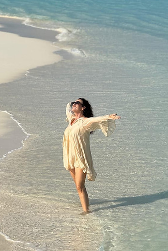 Katrina Valente bare foot on the beach with her toes in the sea and her hands in the air